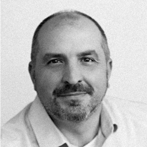 Headshot of lee Swem. He smiles softly, leaning towards the camera. He wears a light-colored button up.